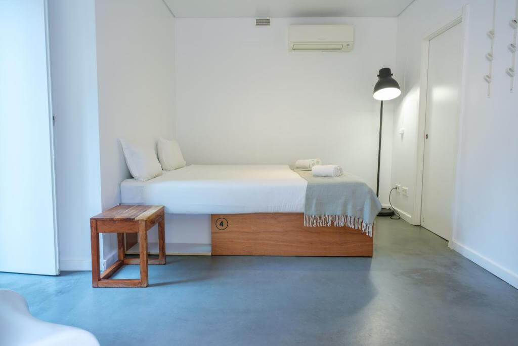 Minimalist white room featuring a modern low-profile double bed and wooden stool.
