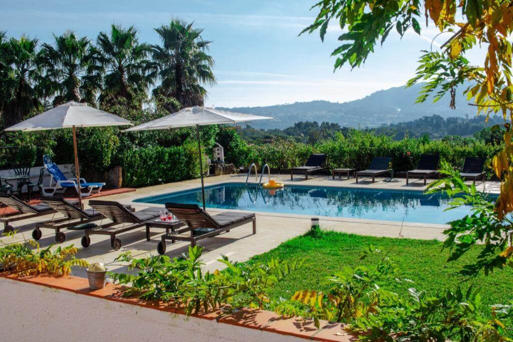 Outdoor swimming pool with lounge chairs and umbrellas overlooking mountains.