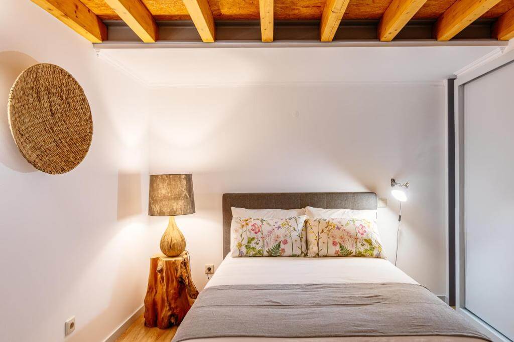 Stylish bedroom with a floral pillow accent, wooden log side table, and warm lamp.