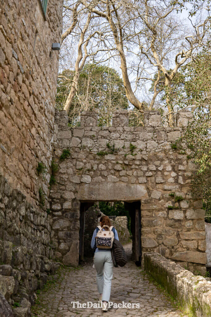 A traveler walks through a historic stone archway entrance at the Moorish Castle in Sintra.
