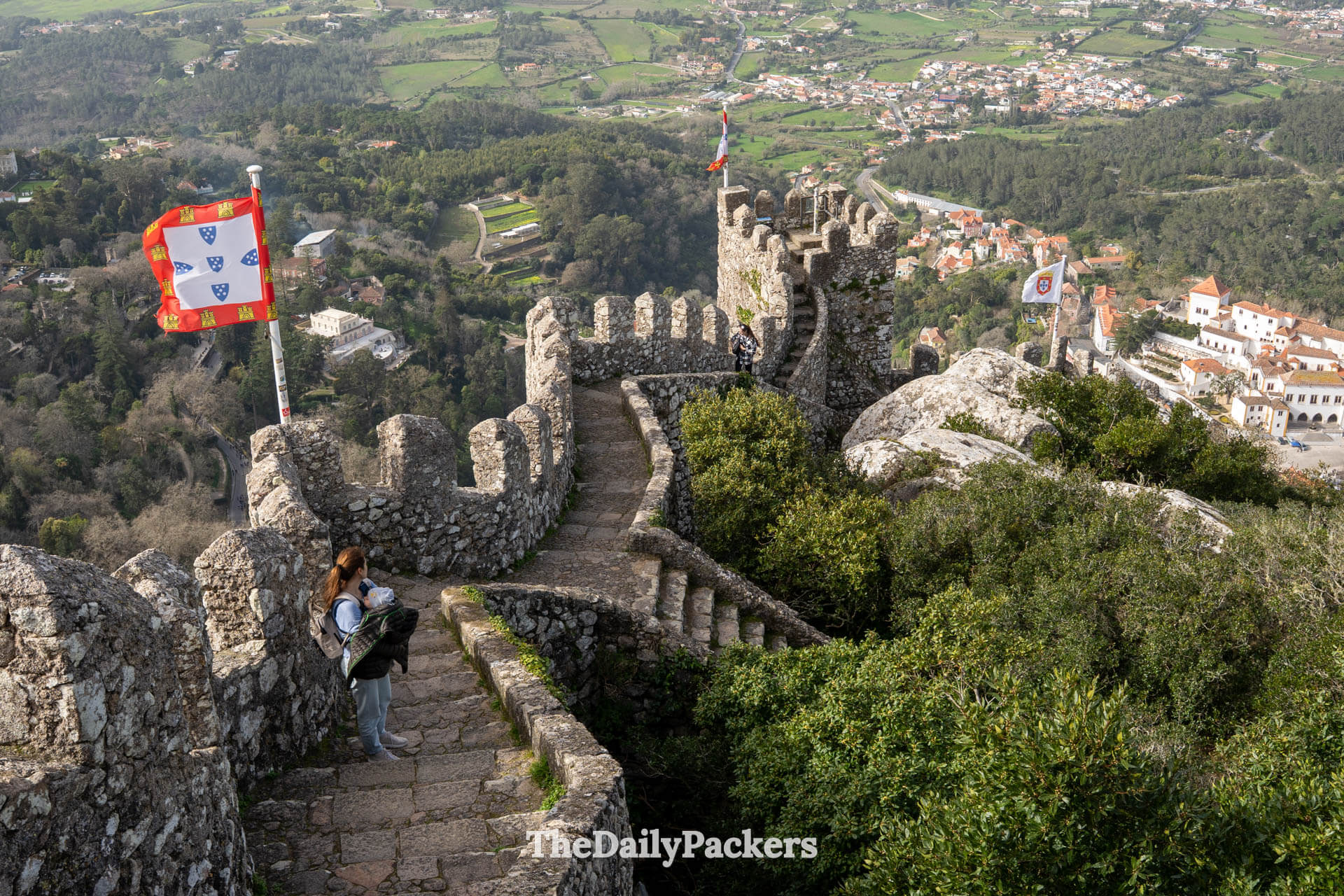 A mother holds her baby on the medieval stone walls overlooking the scenic Sintra valley.