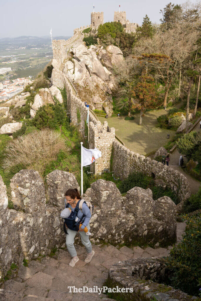 A mother carrying a baby climbs the steep stone stairs along the Moorish Castle ramparts.