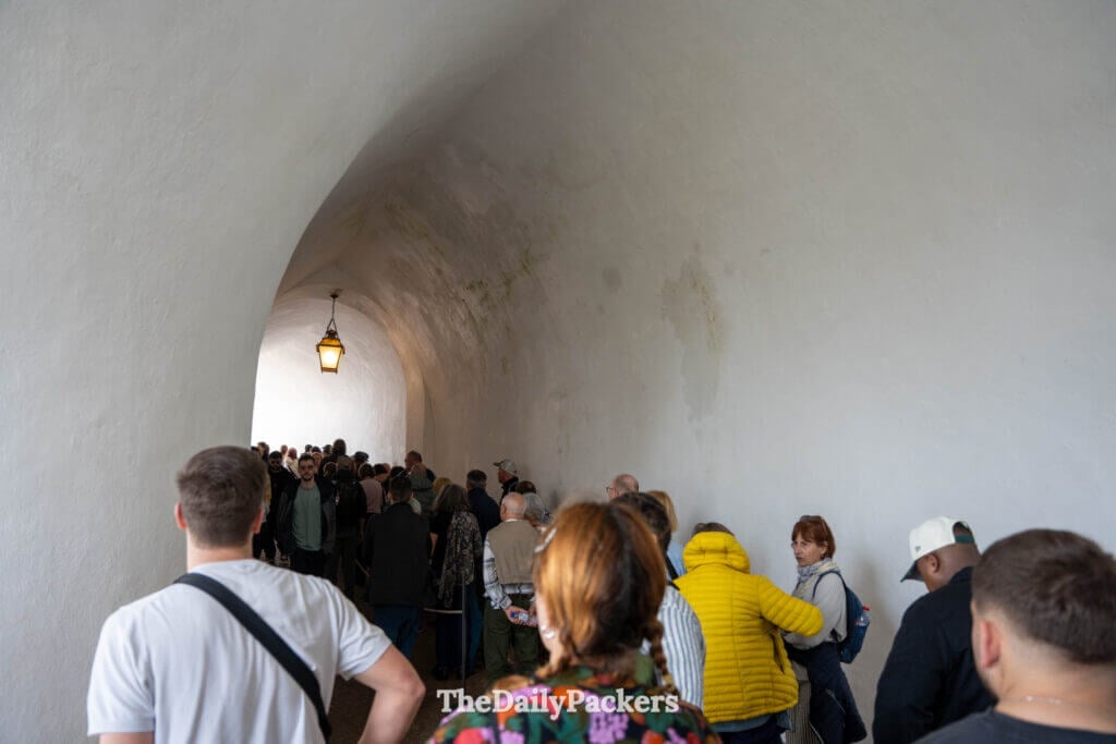 Tourists waiting in a long line under a stone archway tunnel inside Pena Palace in Sintra.
