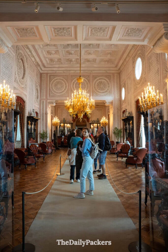 Visitors walking through a grand ballroom inside Pena Palace beneath a large gold chandelier.