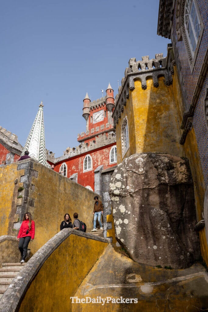 Tourists walking down yellow stone steps with the red clock tower in the background.