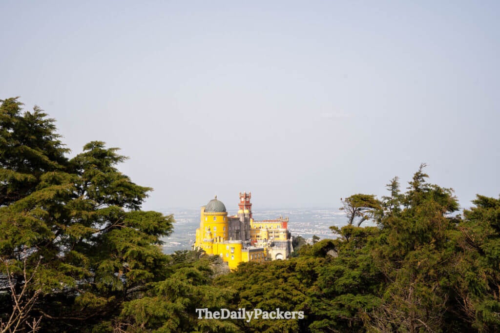 Distant view of the colorful Pena Palace towers framed by lush green forest trees.